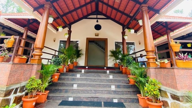 A staircase leading to a covered entrance with a red roof, flanked by potted plants and a stone wall. - Commune Homes Chikmagalur (Chikkamagaluru)