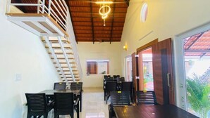 A spacious dining area with high ceilings and a staircase leading to an upper level. - Commune Homes Chikmagalur (Chikkamagaluru)