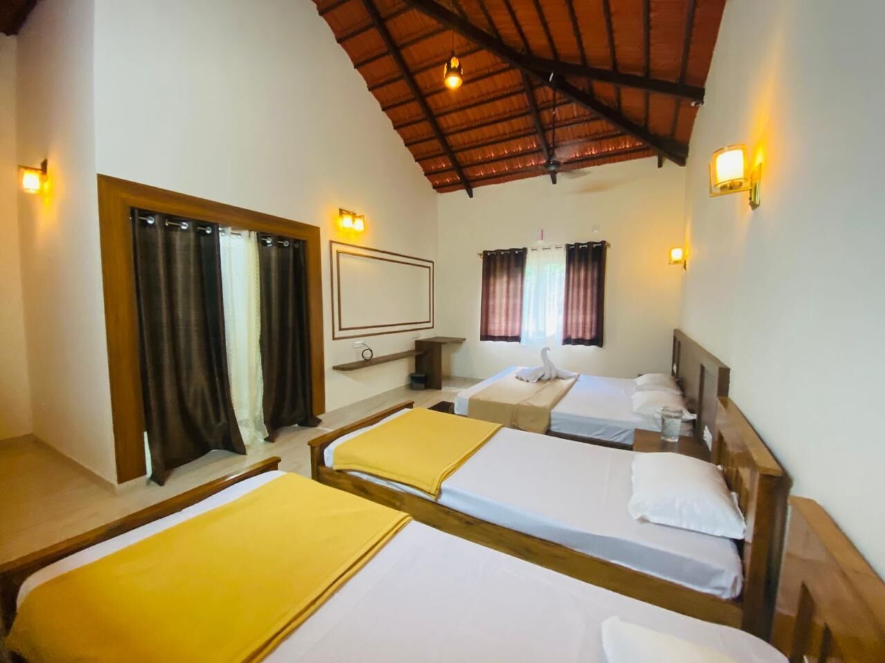 A hotel room with three single beds, a wooden ceiling, and two wall-mounted lamps.