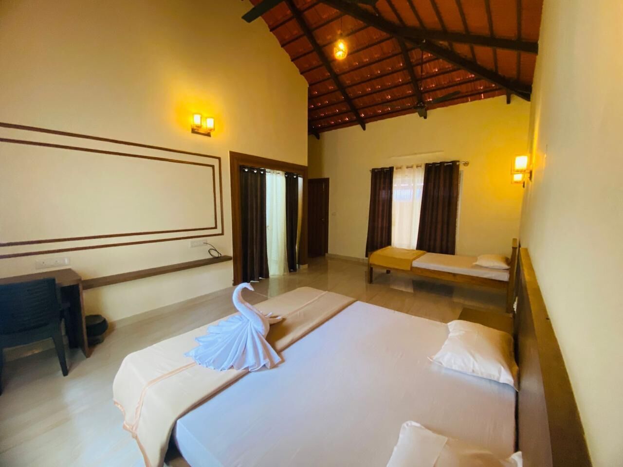 A hotel room with two beds, a desk, and a large window with curtains.