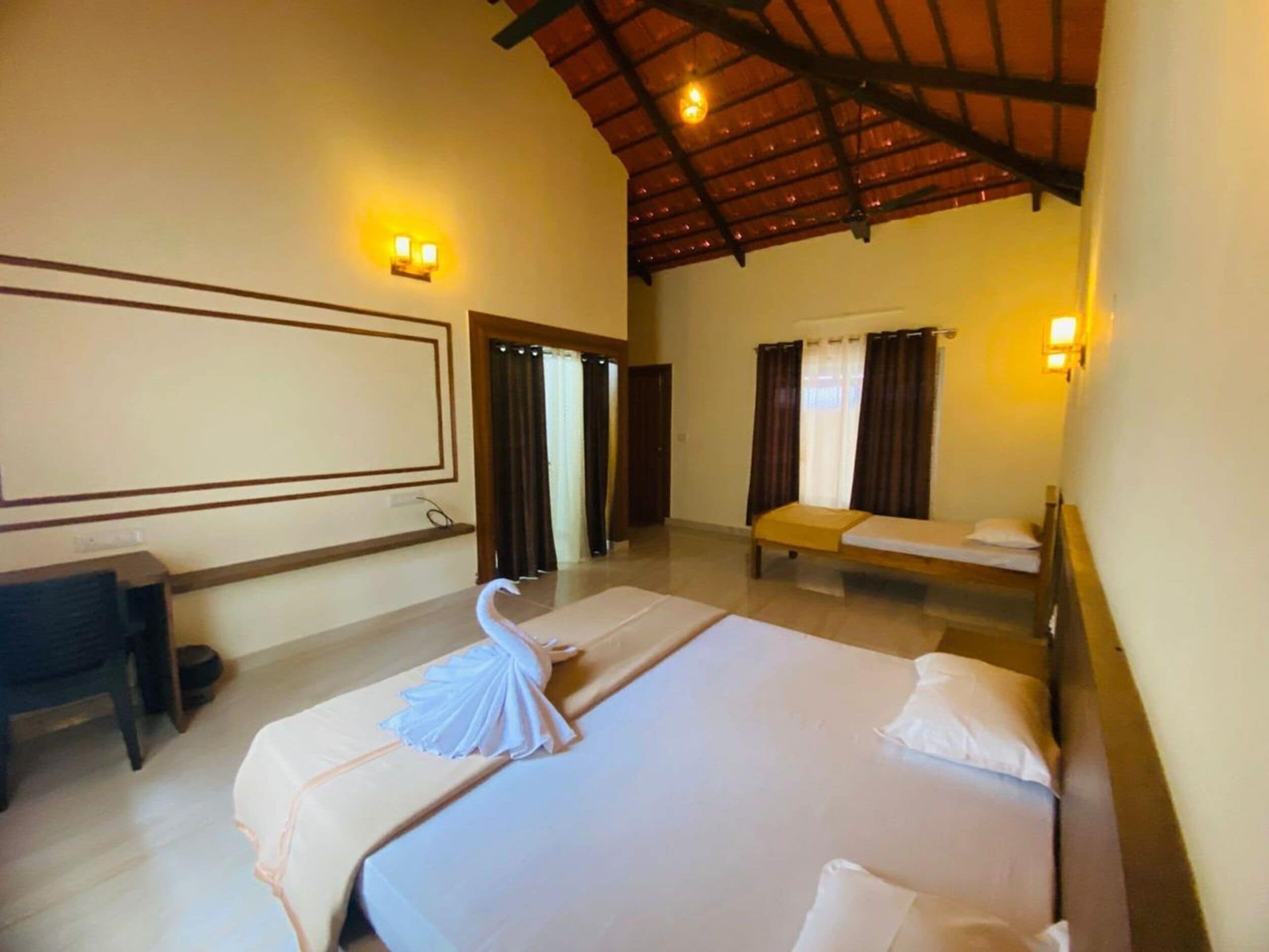 Une chambre d’hôtel avec un grand lit, un bureau et une chaise. Il y a deux fenêtres avec des rideaux.
