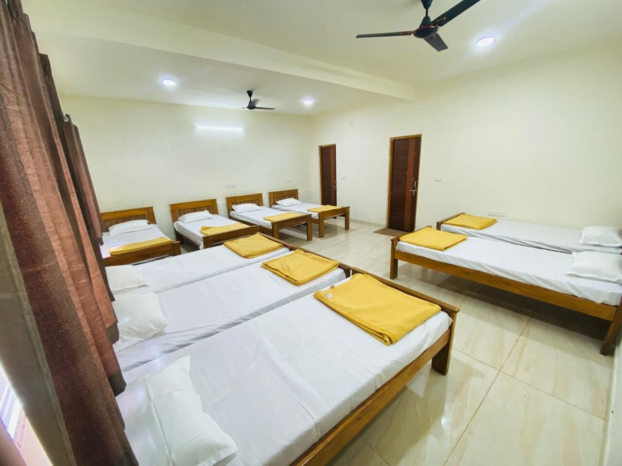 Habitación de hotel con varias camas individuales, cabeceros de madera y un ventilador de techo.