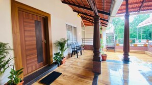 A covered outdoor area with wooden flooring, a wooden door, and potted plants. - Commune Homes Chikmagalur (Chikkamagaluru)