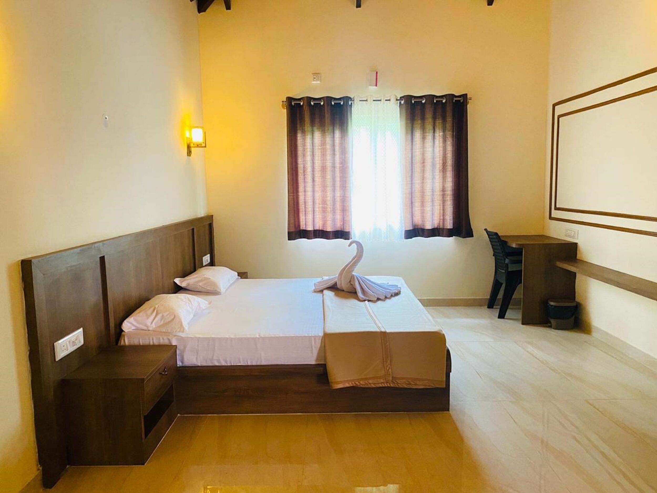 Habitación de hotel con una cama de madera, una mesita de noche, un escritorio y un ventanal con cortinas.