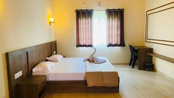 Habitación de hotel con una cama de madera, una mesita de noche, un escritorio y un ventanal con cortinas.