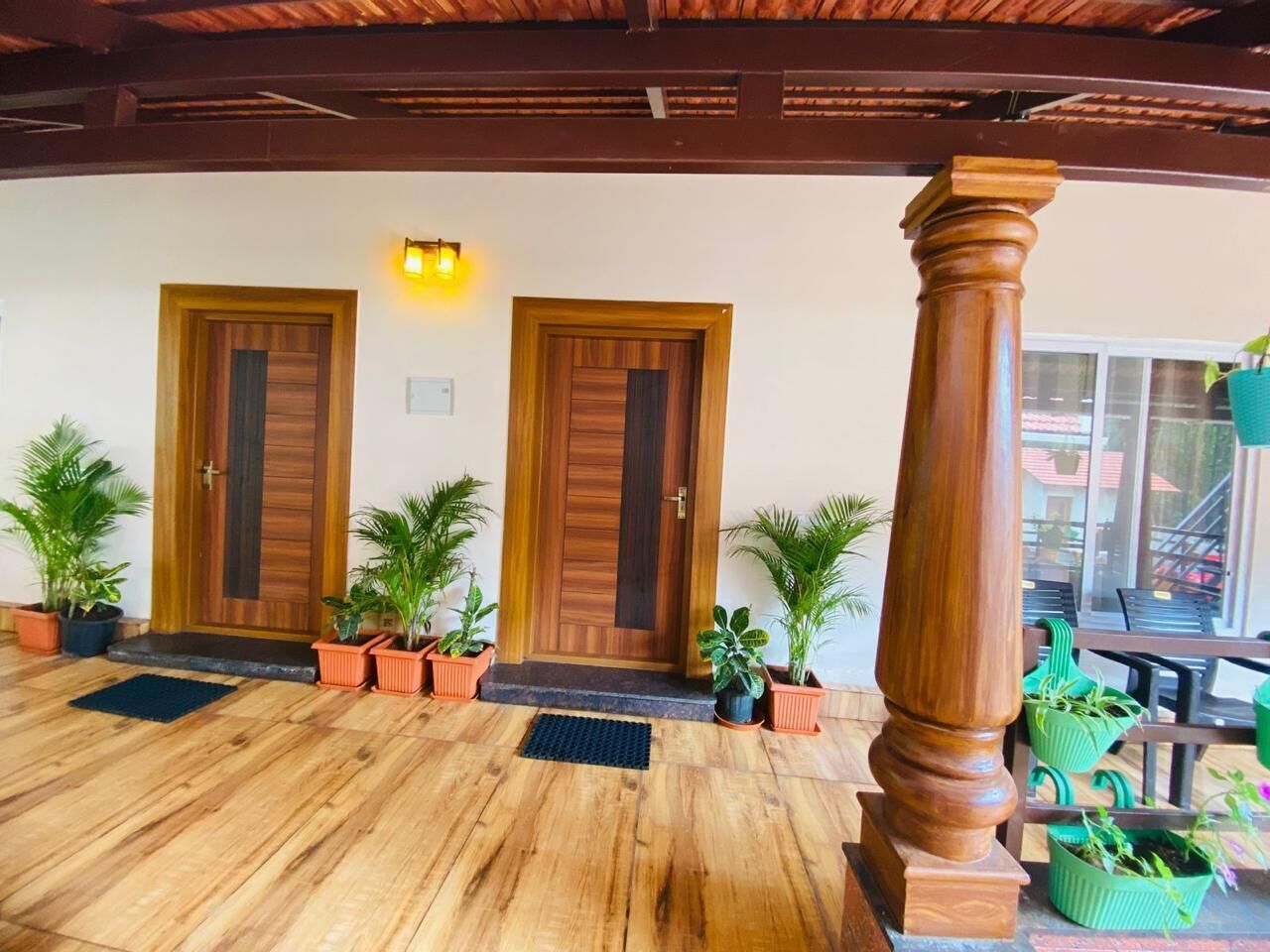 A wooden-floored entrance with two wooden doors, potted plants, and a wooden column.