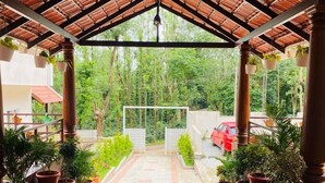 A covered outdoor area with a tiled floor, potted plants, and a red carpet leading to a gate. - Commune Homes Chikmagalur (Chikkamagaluru)