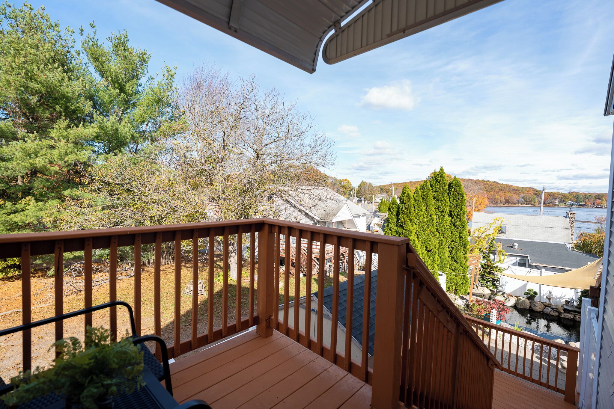 A wooden deck with a view of a lake, trees, and a building in the background.