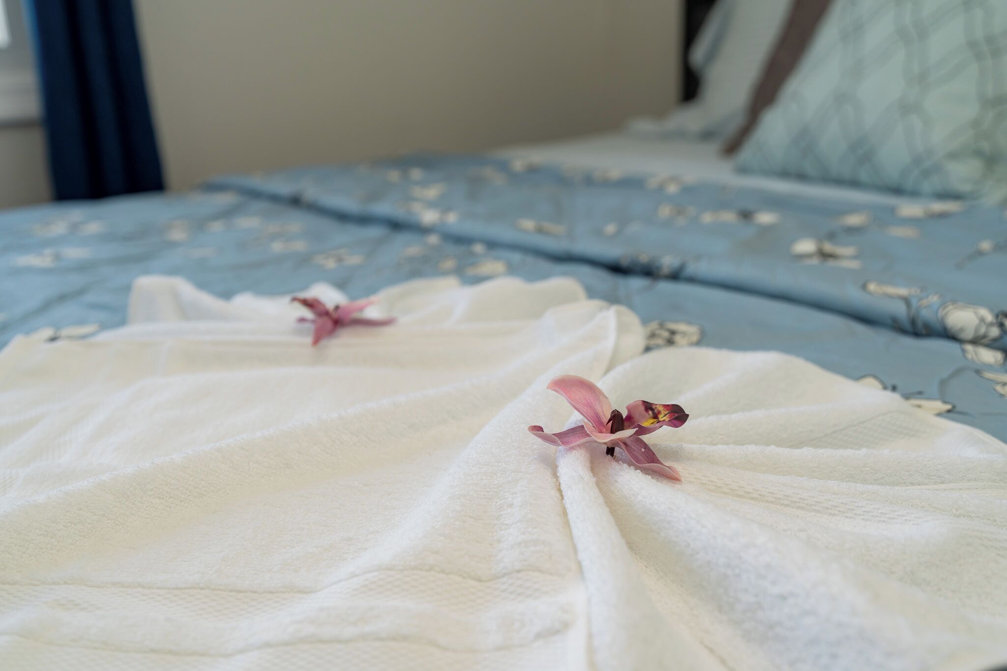 Una cama con una colcha azul estampada con flores y toallas blancas con motivos florales rosados.