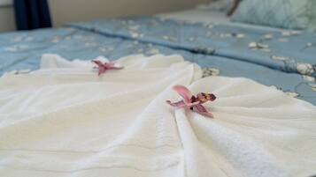 Una cama con una colcha azul estampada con flores y toallas blancas con motivos florales rosados.