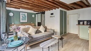 Un salon confortable avec un canapé, une table à manger avec des assiettes et des verres, un banc et un coin cuisine équipé d’une machine à café.