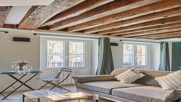 Un salon chaleureux avec un plafond en bois, un canapé, une table basse et un coin repas comprenant des chaises et une table.