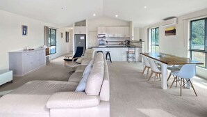 Una sala de estar moderna con sofá, comedor, cocina y ventanas amplias.