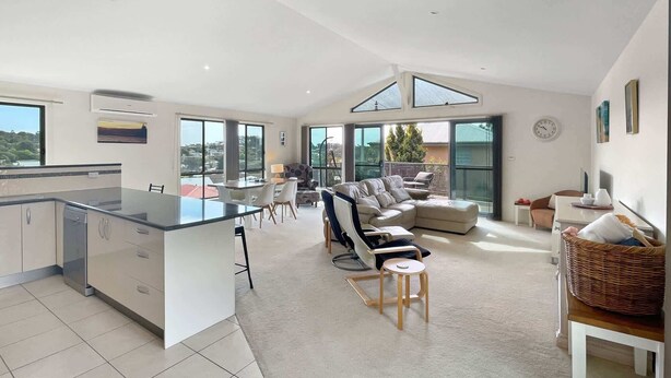 Una cocina moderna con una isla central, un comedor con sofá y sillas, y una sala de estar con un amplio sofá modular.
