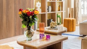 A modern living room with a wooden floor, a round coffee table, and a vase of flowers. - Merveil Signature Suite - Archives II (Paris)
