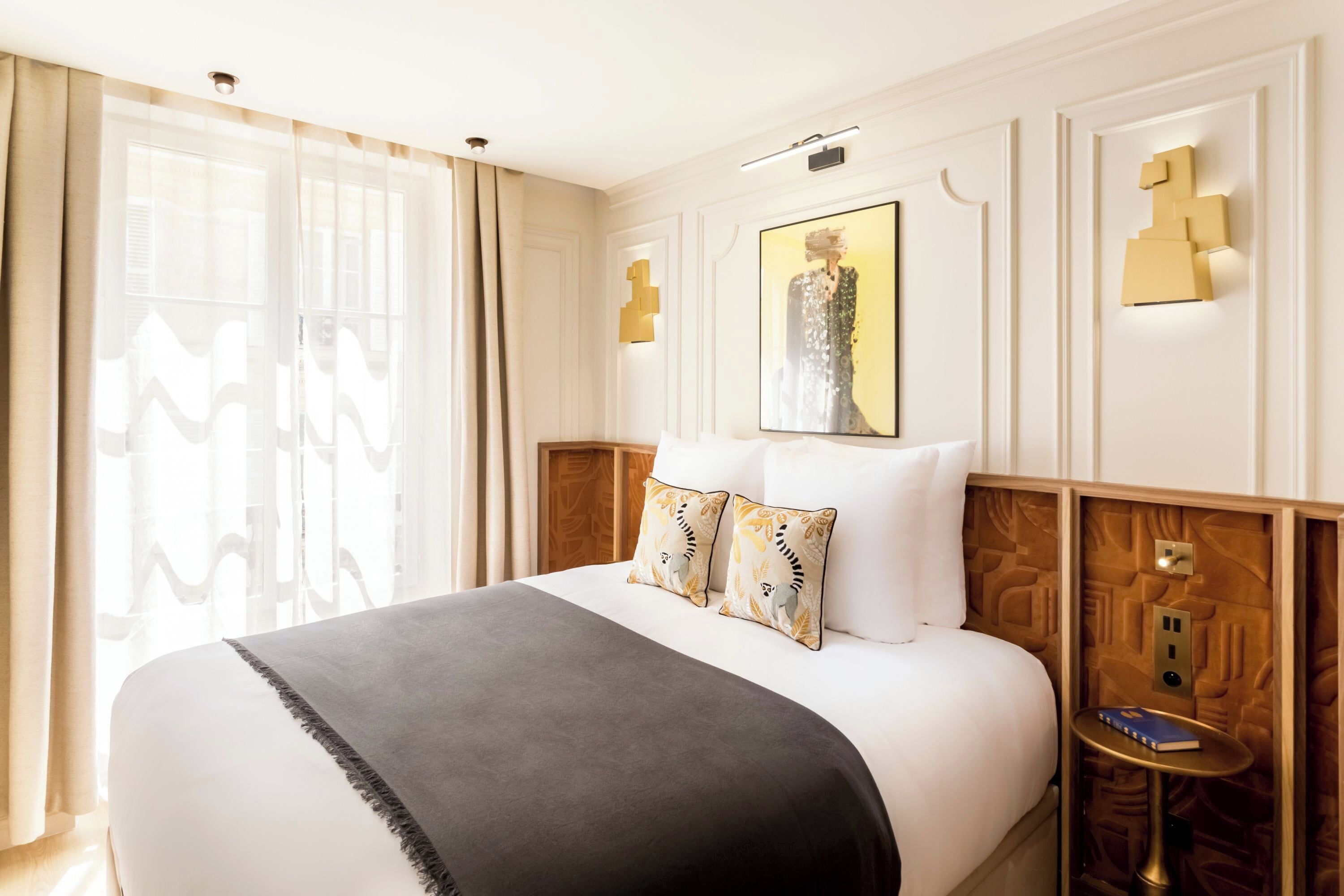 Una habitación de hotel con una cama grande, una mesita de noche, una lámpara de pared y una obra de arte enmarcada sobre la cama.