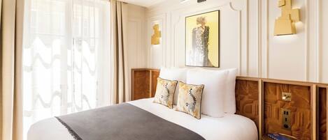 Una habitación de hotel con una cama grande, una mesita de noche, una lámpara de pared y una obra de arte enmarcada sobre la cama.