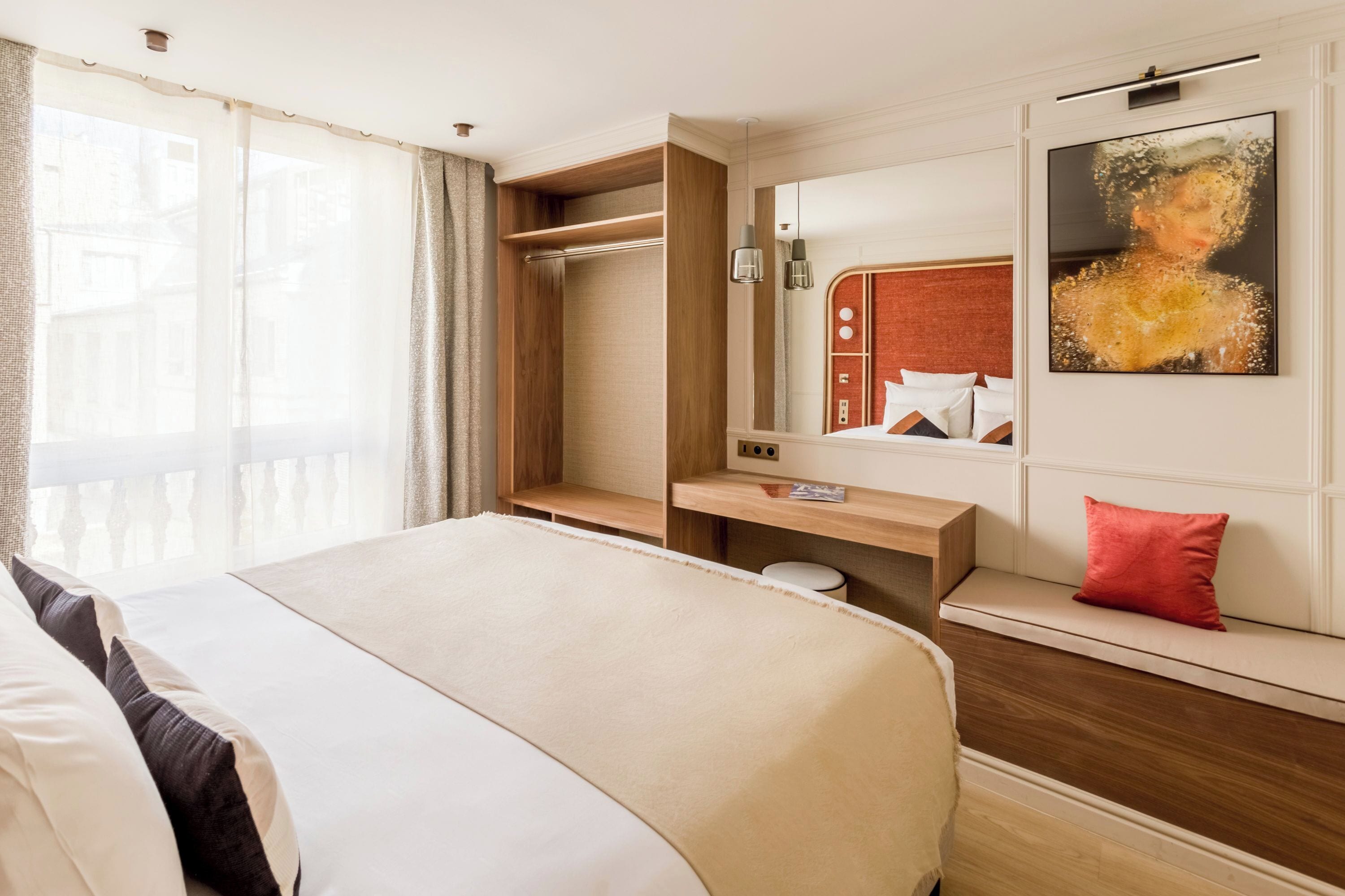 Ein Hotelzimmer mit Bett, Holzschreibtisch, einer Bank, einem Spiegel und einem Gemälde.