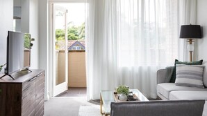 A modern living room with a television on a wooden cabinet, a sofa with cushions, a coffee table, and a lamp. - Sunny Apartment in Quiet and Green Neighbourhood (Sydney)