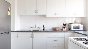 A modern kitchen with white cabinets, a granite countertop, a microwave, and a stove. - Sunny Apartment in Quiet and Green Neighbourhood (Sydney)