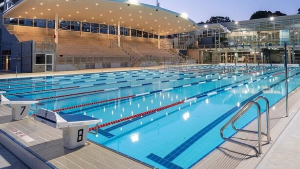 A large indoor swimming pool with multiple lanes, a covered spectator area, and a modern building with large windows. - Sunny Apartment in Quiet and Green Neighbourhood (Sydney)
