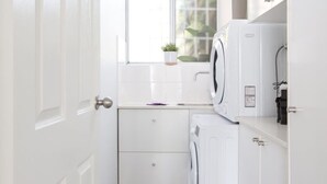 A compact laundry room with a washing machine, dryer, and a small window with a plant. - Sunny Apartment in Quiet and Green Neighbourhood (Sydney)
