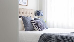 A neatly made bed with a tufted headboard, a patterned throw blanket, and a bedside lamp with a floral design. - Sunny Apartment in Quiet and Green Neighbourhood (Sydney)