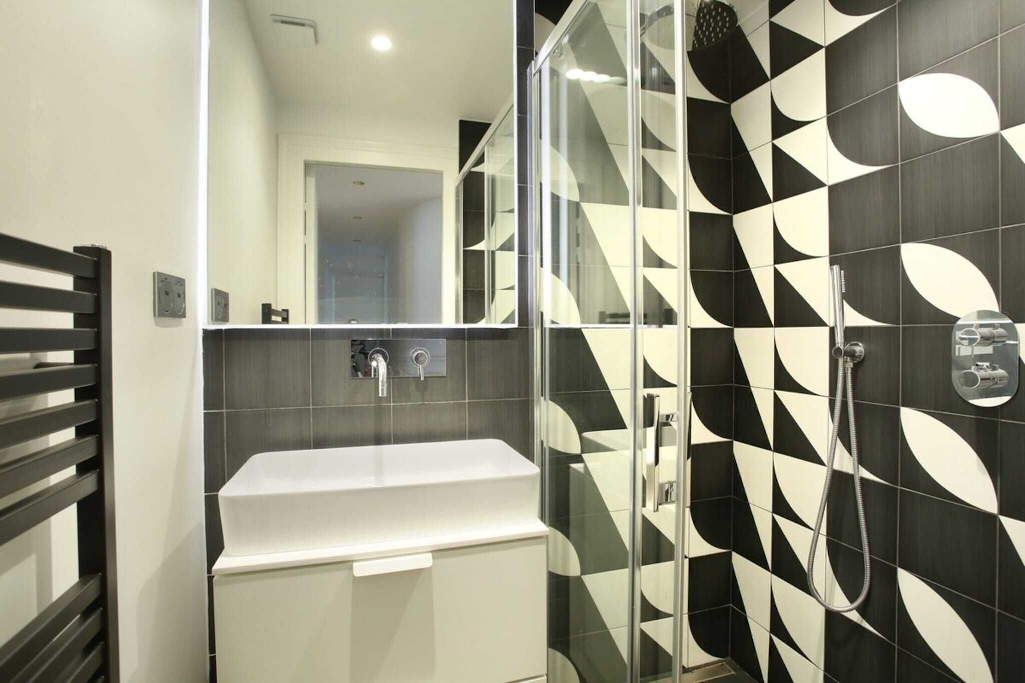 Une salle de bain moderne avec une douche à parois de verre, un lavabo blanc et un mur orné d’un motif géométrique.