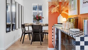 A dining area with a round table, black chairs, and a vase with flowers. There are framed mirrors on the wall and a decorative vase with pampas grass. - Charming Forrestfield Escape! (Forrestfield)