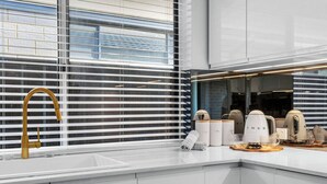 A modern kitchen with a gold faucet, white cabinets, and a window with blinds. - Charming Forrestfield Escape! (Forrestfield)
