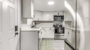 Eine kleine Küche mit weißen Schränken, einer Mikrowelle, einem Backofen und einem Kühlschrank.