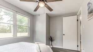 Ein Schlafzimmer mit einem Bett, einem Deckenventilator, einem Fenster und einer Tür.