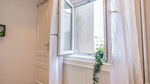 A room with a white door, a window with a white curtain, and a plant on the windowsill. - Comfy 2BR Apt Long Stay Matzleinsdorfer (Vienna)