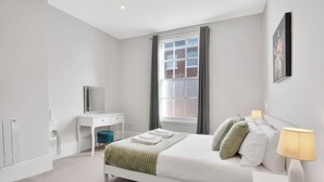 A bedroom with a bed, bedside table, lamp, and a window with curtains. - WhiskAwayHomes Shaw Street Apartment 6 (Worcestershire)