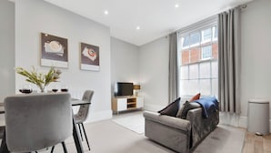 A modern living room with a grey sofa, a dining table with chairs, a TV, and artwork on the wall. - WhiskAwayHomes Shaw Street Apartment 6 (Worcestershire)