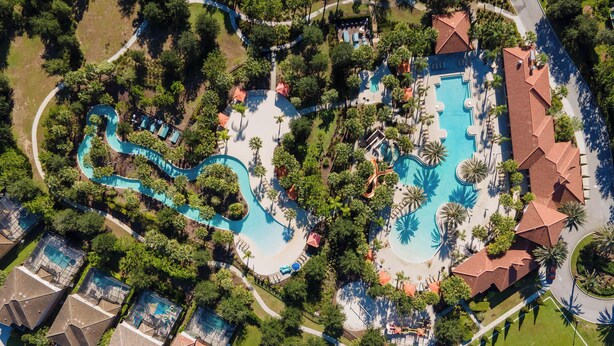 Vue aérienne d’un complexe hôtelier doté de plusieurs piscines, de palmiers et d’un court de tennis.