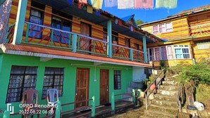 A colorful two-story building with a green facade, wooden balconies, and a staircase leading to the upper floor. - Paradise Homestay (Kalimpong)