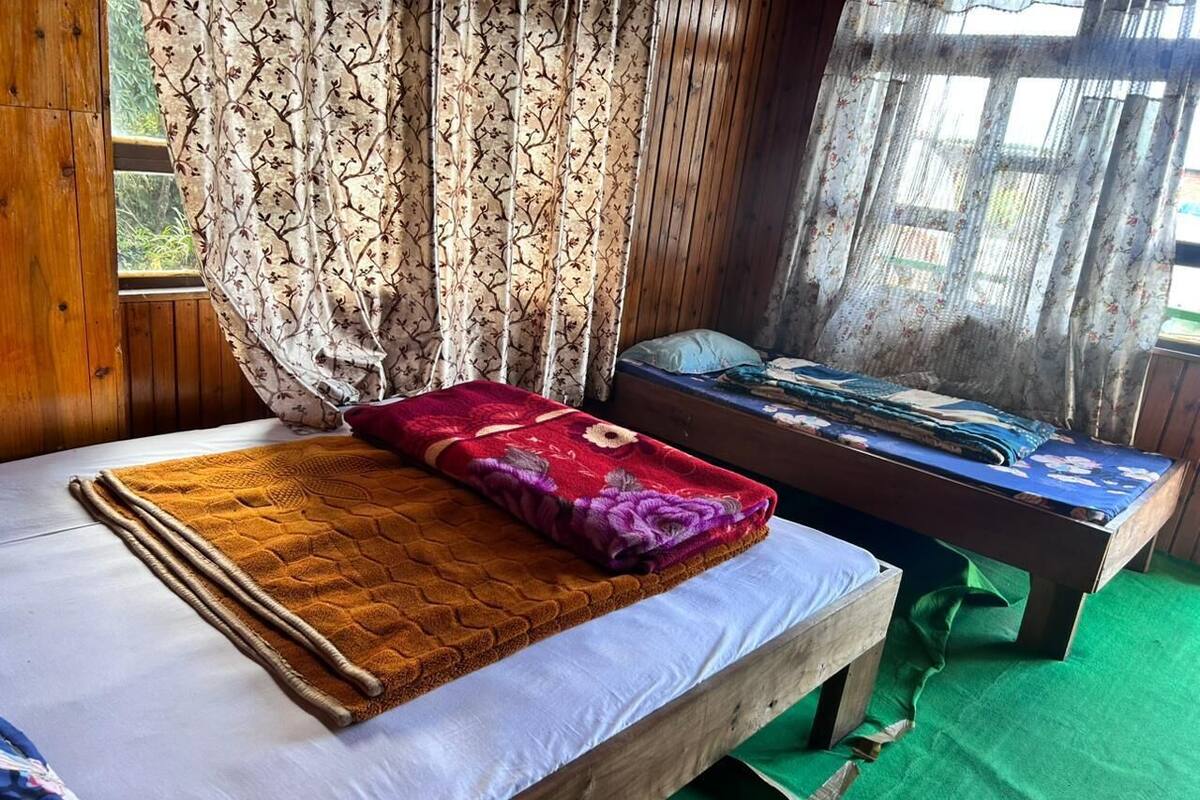 Un lit en bois avec un matelas blanc, une couverture rouge et violette, et un tapis vert sur le sol.