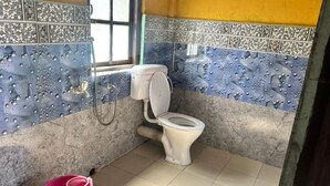 A small bathroom with a toilet, a pink bucket, and tiled walls. - Paradise Homestay (Kalimpong)