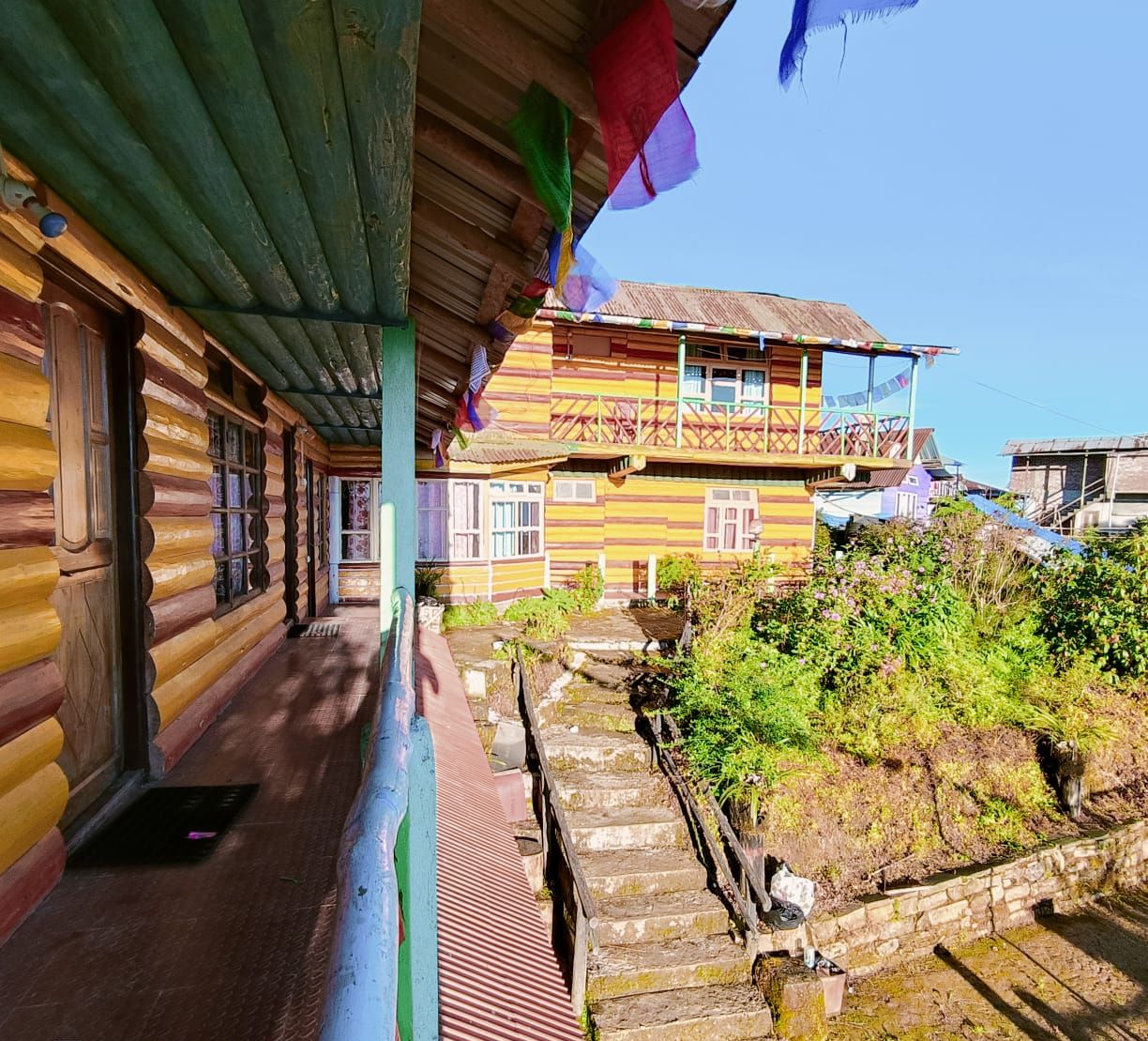 A traditional wooden house with a balcony, a staircase leading to a higher level, and a clear sky.
