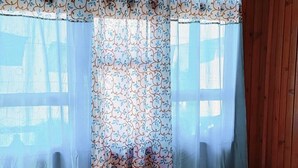 A single bed with a white mattress and a red blanket, a wooden headboard, and a window with patterned curtains. - Paradise Homestay (Kalimpong)