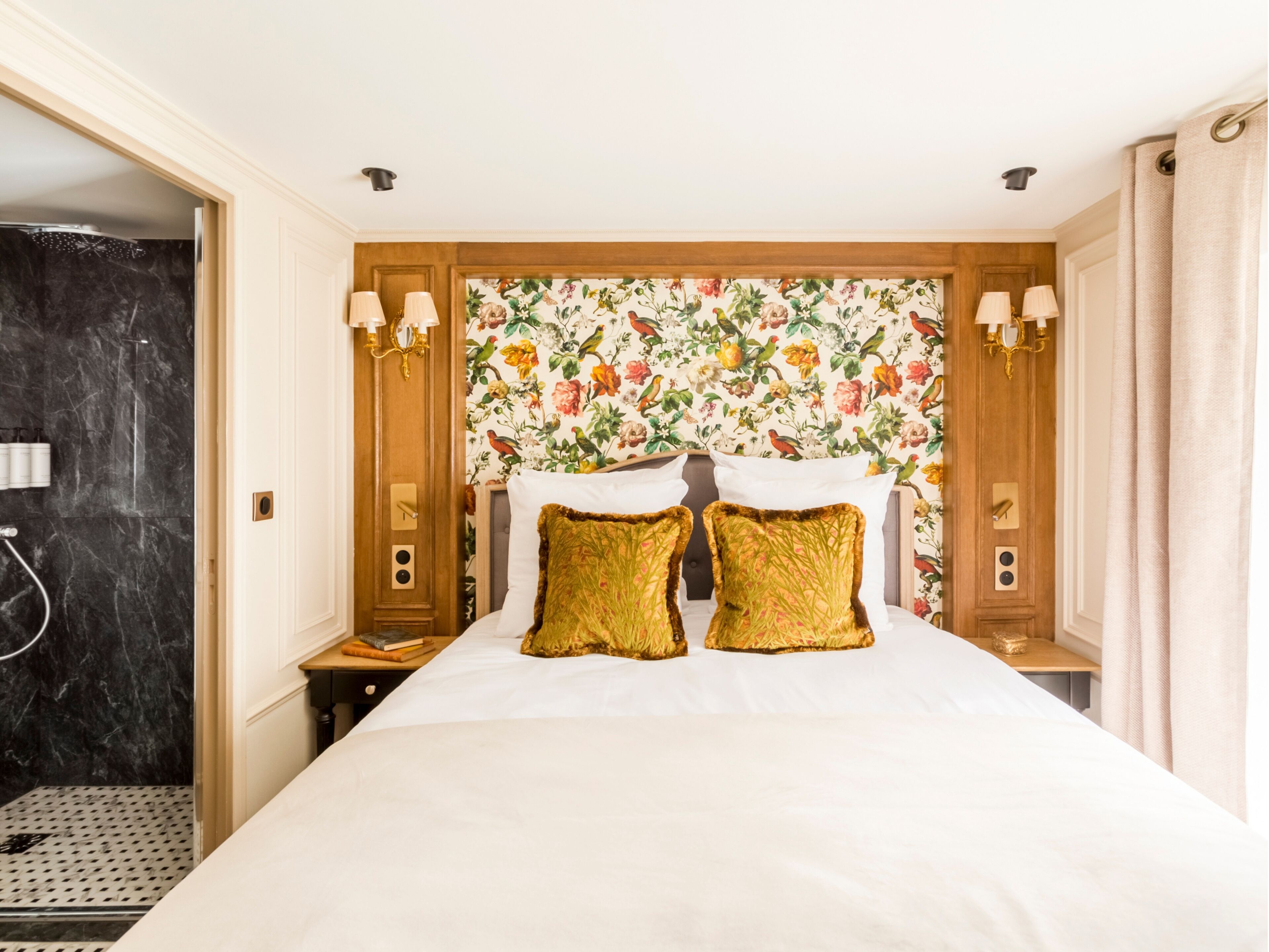 A hotel room with a large bed, floral wallpaper, two bedside lamps, and a wooden headboard.