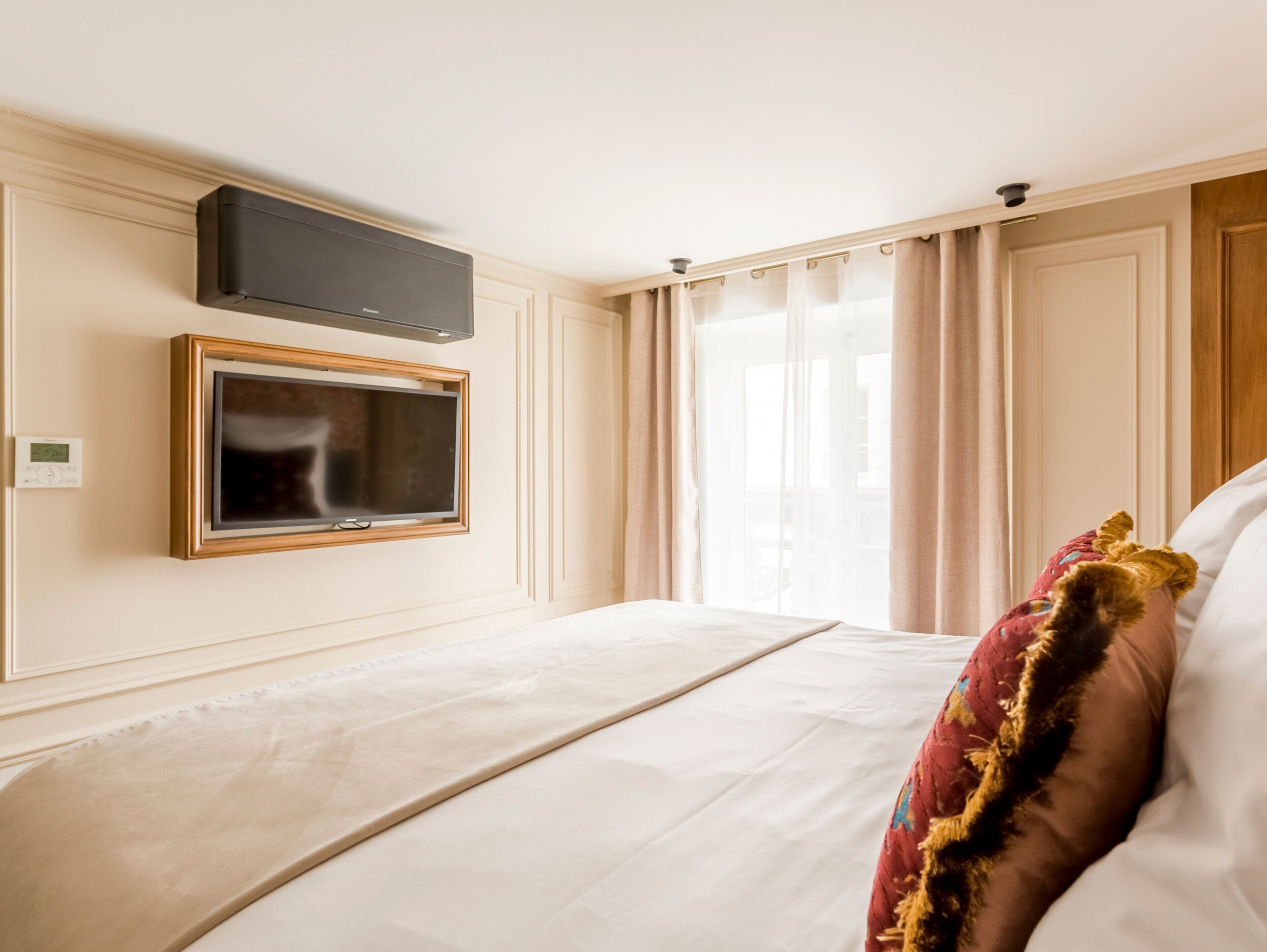 Quarto de hotel com cama, televisão fixada na parede e janela com cortinas.