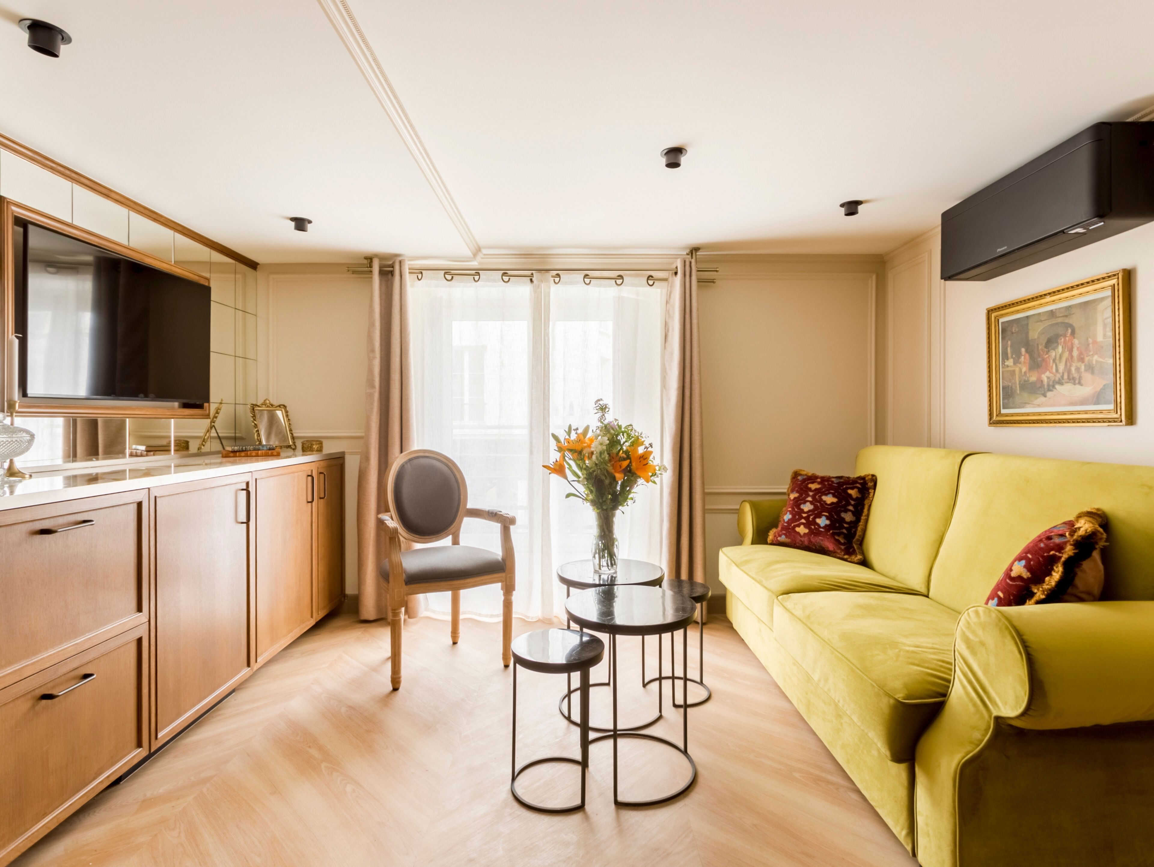 Een moderne woonkamer met een geel sofa, een eettafel en een aan de muur bevestigde televisie.