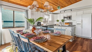 A modern kitchen with white cabinets, a wooden ceiling, and a dining area with a wooden table and blue chairs. - Ocean Views • Private Pool • Walk to Beach (St. Augustine)