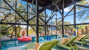 An indoor pool area with clear views of trees and a building in the background, surrounded by lounge chairs and a floating flamingo decoration. - Ocean Views • Private Pool • Walk to Beach (St. Augustine)