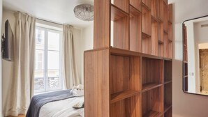 A bedroom with a bed, a wooden wardrobe, a window with curtains, and a ceiling light fixture. - New Apartment Center of Paris Le Marais (Paris)