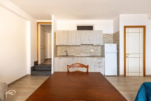 Una cocina compacta con microondas integrado, refrigerador y lavamanos. En primer plano, hay una mesa de comedor con una silla.