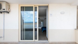 Une chambre d’hôtel dotée d’une porte-fenêtre coulissante donnant sur un balcon, avec le numéro « 7 » bien visible sur le mur, et un petit climatiseur fixé au mur.