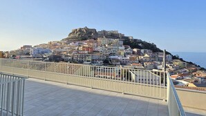 Une ville côtière avec un fort imposant situé sur une colline, des immeubles résidentiels et un ciel dégagé.